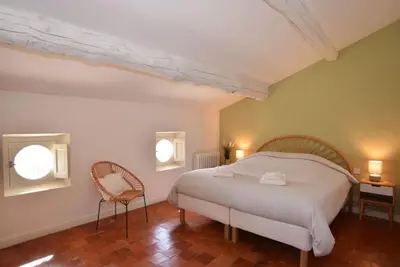 a bedroom with a bed and a chair and two windows at L'Atelier Appartement au cœur du vignoble in Rognes