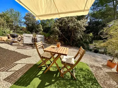 a wooden table and two chairs under an umbrella at Paisible studio tout neuf en lisière de forêt in Peyrolles-en-Provence