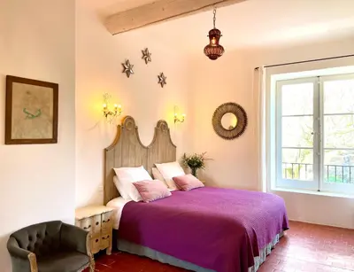 a bedroom with a bed with a purple bedspread and a chair at La Grande Verrière - Luberon en Provence in Goult