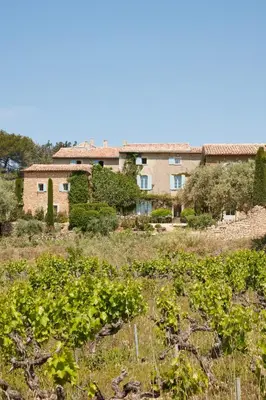 a building in the background with a field of plants at La Bastide du Mourre - Fontenille Collection in Oppède