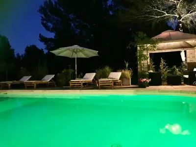a swimming pool with two chairs and an umbrella at Gîte de charme La Manola in Rognes