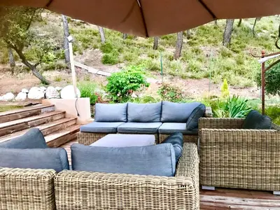 a patio with wicker chairs and couches and an umbrella at Chambres d'hôtes La Manola in Rognes