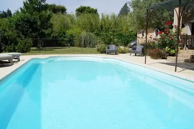 a large blue swimming pool with two chairs and an umbrella at villa entre st rémy de provence et avignon in Noves