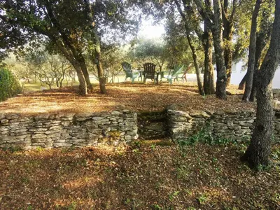 a stone wall and a bench in a park with trees at Le Fiacre entre chênes et oliviers dans le Luberon in Cabrières-dʼAvignon