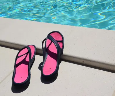 a pair of pink and black flip flops next to a swimming pool at Ici et Là - Chambres d'hôtes in Velleron