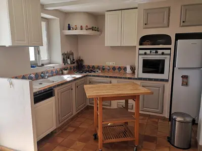 a kitchen with white cabinets and a wooden table at Les Vendangeurs, gîte au milieu des vignes face au Luberon in Goult