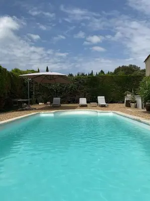 a large blue swimming pool with an umbrella and chairs at Maison avec ses 2 terrasses et sa piscine in Eyragues