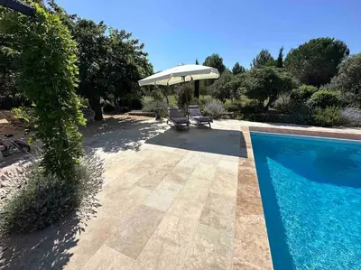 a pool with an umbrella and chairs next to a house at Mas de charme avec piscine au coeur des Alpilles in Eygalières