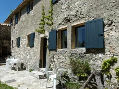 a stone building with blue shutters and a table and chairs at Provencal farmhous Lubéron, swimming pool in Revest-des-Brousses