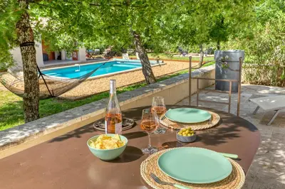 a table with two plates of food and wine and a pool at Gite neuf avec piscine Bio uv in Saint-Saturnin-les-Apt