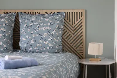 a bed with a blue comforter and a table with a lamp at L'Isle en Blanc - 4 couchages - Hypercentre - Clim - Wifi in LʼIsle-sur-la-Sorgue