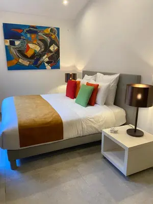 a bedroom with a bed with colorful pillows and a table at La RENAUDIERE in LʼIsle-sur-la-Sorgue
