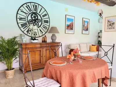 a living room with a table with a large clock on the wall at LUBERON SOLEIL ET OLIVIERS in Les Taillades