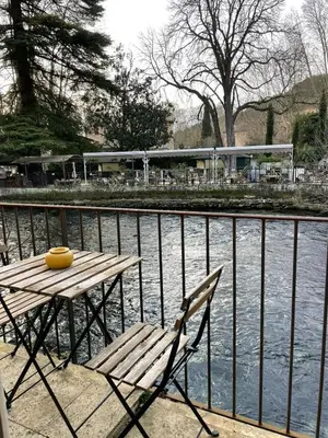 a wooden table and chair next to a body of water at Jacuzzi & Terrasse en bord de rivière in Fontaine-de-Vaucluse