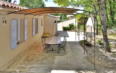 a patio with a table and chairs under a wooden canopy at La Villa Du Soleil in Lacoste
