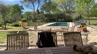 a table with three chairs and a swimming pool at le mas du lavoir in Gordes