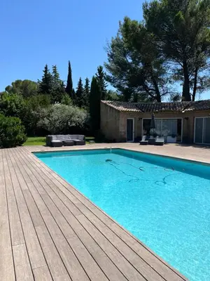a swimming pool with a wooden deck next to a house at Le p’tit bonheur-Piscine chauffée-clim-Park in Carpentras