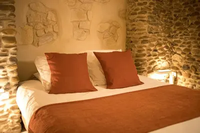 a bedroom with a bed with pillows and a stone wall at In Provence Hôtel - Expérience Authentique in Venelles