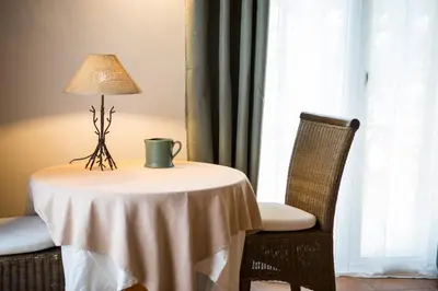 a table with a lamp and a chair next to a window at In Provence Hôtel - Expérience Authentique in Venelles