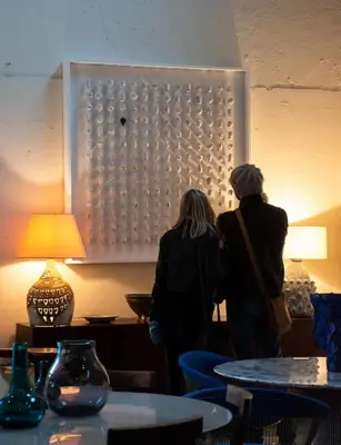 two people standing in a room with tables at Une pause en Provence au Village des antiquaires de la Gare in LʼIsle-sur-la-Sorgue