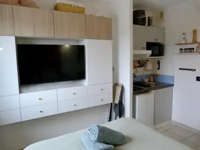 a kitchen with white cabinets and a large flat screen tv at Charmant studio le clos d'Aix parking privé gratuit et piscine in Aix-en-Provence