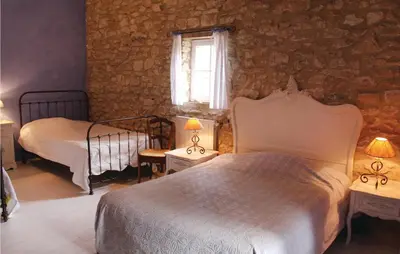 a bedroom with two beds and a stone wall at Belle Maison À Lacoste in Lacoste