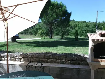a patio with a table and an umbrella and a yard at Le Pas des Lanciers in Mallemort