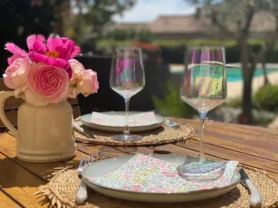 a table with two glasses and plates and a vase with flowers at Au pied du luberon in Pertuis