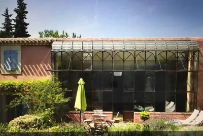 a greenhouse in a yard with a table and an umbrella at Ecolodge Au fil de l'eau, avec piscine intérieure et parc arboré in Lagnes