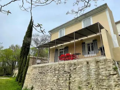 a house with a stone wall and red chairs on a balcony at Villa luxueuse à Ménerbes + piscine in Ménerbes
