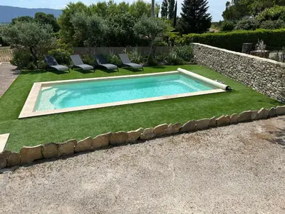 a swimming pool in a yard with chairs and grass at Les Juliens in Gordes