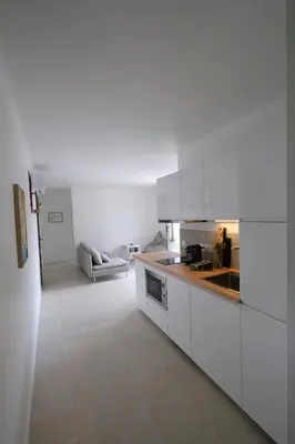 a kitchen with white cabinets and a living room at Rouleraventoux, Gîte sportif avec piscine, sauna, salle de sport, jardin in Mormoiron