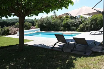 a patio with two chairs and an umbrella next to a swimming pool at Air-conditioned house in the Luberon with heated swimming pool in Saint Saturnin les Apt - 8 people. in Saint-Saturnin-les-Apt