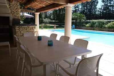 a table and chairs on a patio with a swimming pool at Provencal Farm with swimming pool near Isle sur la Sorgue - 10 people. in Les Vignères