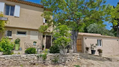 a house with a tree and a stone wall at Le Jardin des Oliviers in Apt