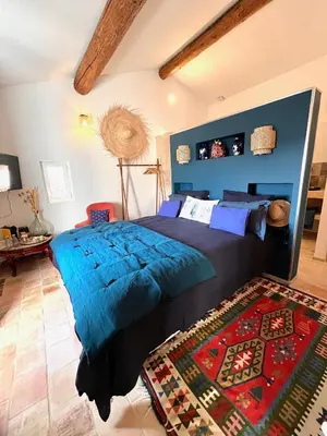 a bedroom with a bed with a blue blanket and a rug at Le Mas d'Emilienne in Coudoux