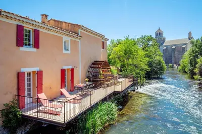 a bridge over a river next to a building at Ancien Moulin avec piscine proche Isle-sur-Sorgue in Le Thor