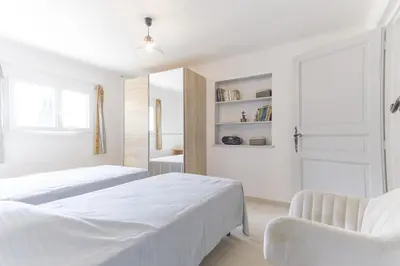 a white bedroom with two beds and a chair at Le Petit Nid in Saint-Rémy-de-Provence