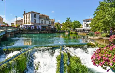 a river with a waterfall in a town with flowers at Nice Apartment In L'isle-Sur-La-Sorgue in LʼIsle-sur-la-Sorgue
