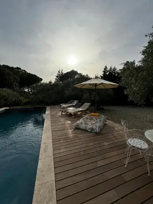 a wooden deck with chairs and an umbrella next to a pool at Les Feuilleres in LʼIsle-sur-la-Sorgue
