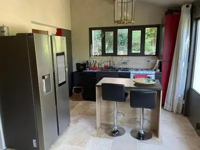 a kitchen with a refrigerator and a counter with two stools at Charmante Maison au cœur du village in Rustrel