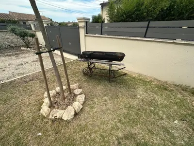 a grill sitting in a yard next to a fence at Maison Isle sur la sorgue in LʼIsle-sur-la-Sorgue
