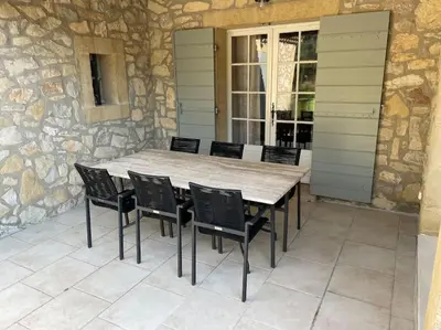 a table and chairs on a patio with a stone wall at Bastide Farandole in Eygalières