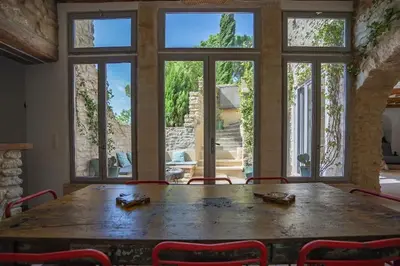 a large wooden table in a room with windows at Maison d'exception au cœur de Goult in Goult