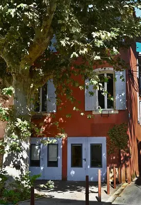 a red building with white doors and a tree at Suite dans maison d'artiste in LʼIsle-sur-la-Sorgue