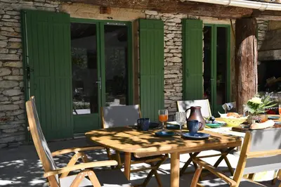 a wooden table and chairs on a patio with green doors at La Piscine dans la Foret in Gordes