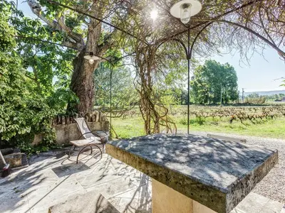 a stone table and a chair under a tree at Charming Cottage in Oppède amidst Vineyards in Maubec