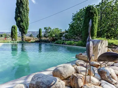 a swimming pool with a statue of a bird next to rocks at Cottage in Oppède with Poolside Bliss in Maubec