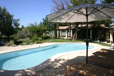 a swimming pool with an umbrella and two chairs and a bench at Villa La Raffinée, au coeur des garrigues du Luberon in Gordes