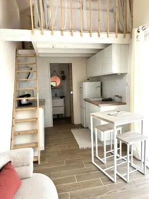 a room with a loft bed with a table and a kitchen at La maisonnette de Tom in Caumont-sur-Durance